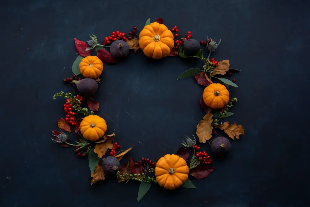 An image of pumpkins, leaves, apricots, and flora formed in the shape of a wreath. 